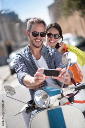 A couple on a scooter in the city, the man takes a selfie © jackfrog