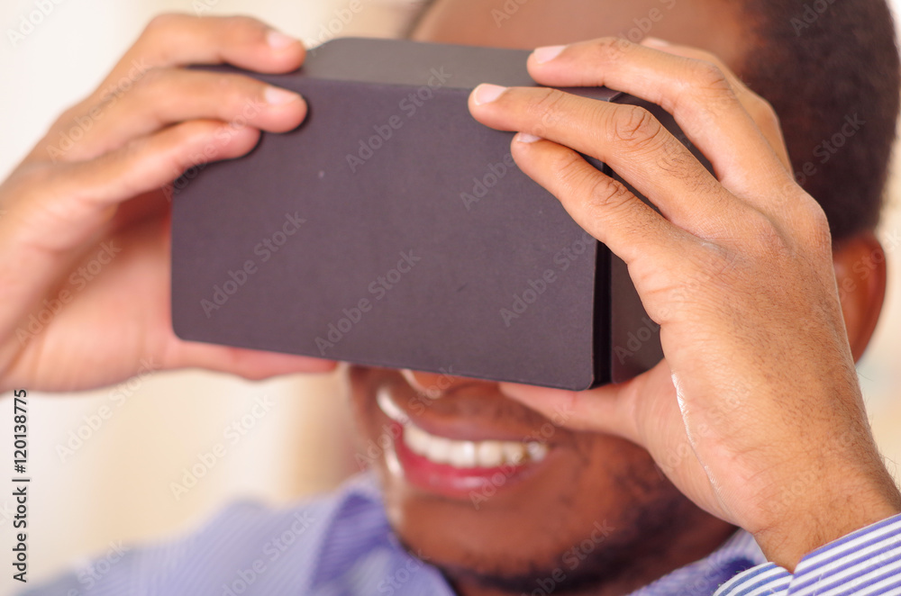 Man wearing blue shirt testing vitrual reality mobile device, holding glasses in front of eyes and smiling Man wearing blue shirt testing vitrual reality mobile device, holding glasses in front of eyes and smiling