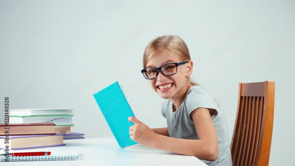 Happy schoolgirl 7-8 years old holding book on her head and smiling at camera Happy schoolgirl 7-8 years old holding book on her head and smiling at camera