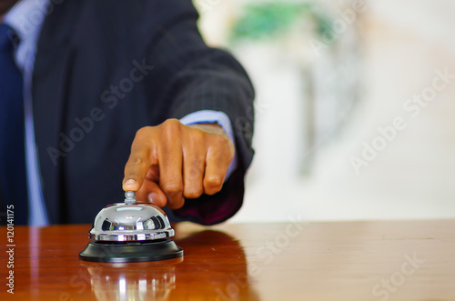 Closeup arm of man wearing blue suit pressing desk bell at hotel reception