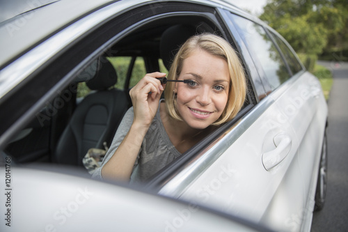 Young blond woman applying makeup while in the car