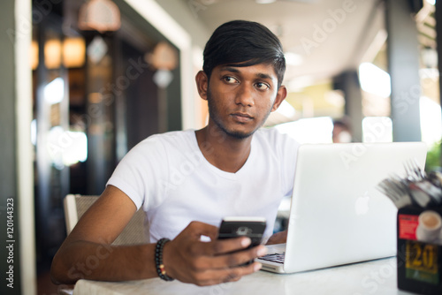 teenage indian male using phone at cafe