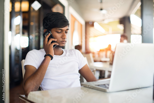 teenage indian male using phone at cafe photo