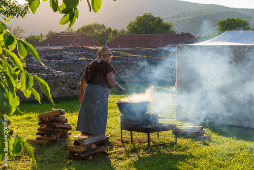 Woman cooking romanian traditional food on fire outdoor in a camping holiday of ulpia traiana, sarmisegetusa, hateg, hunedoara, romania in summer season photo