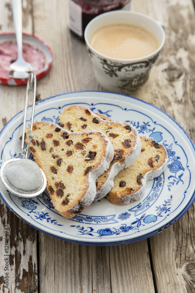Traditional german Stollen with raisins and powdered sugar, on white and blue ceramic plate on wooden table. With espresso and jam. Traditional Christmas baking. Selective focus. Natural light Traditional german Stollen with raisins and powdered sugar, on white and blue ceramic plate on wooden table. With espresso and jam. Traditional Christmas baking. Selective focus. Natural light