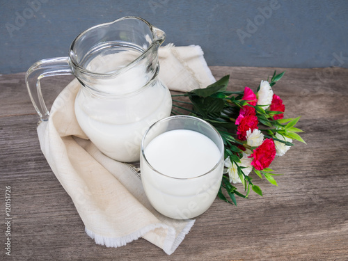 Fresh milk in jug and glass with flower on wooden bqckground photo