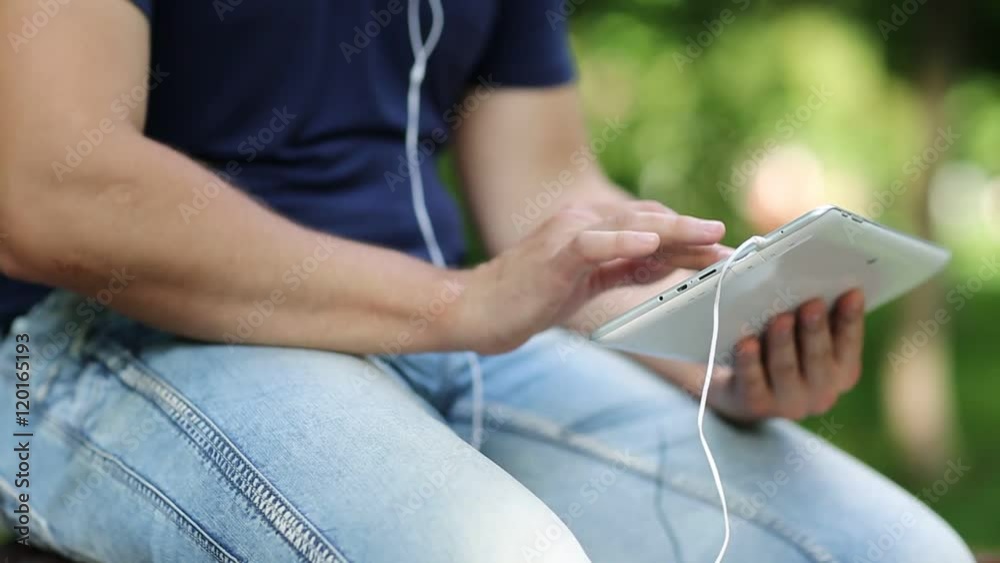 Man looks the photos in his tablet computer. Closeup of man hands with white tablet pc and earphones. Man holds in hands white tablet pc. Man looks and flips through the photos in his computer Man looks the photos in his tablet computer. Closeup of man hands with white tablet pc and earphones. Man holds in hands white tablet pc. Man looks and flips through the photos in his computer