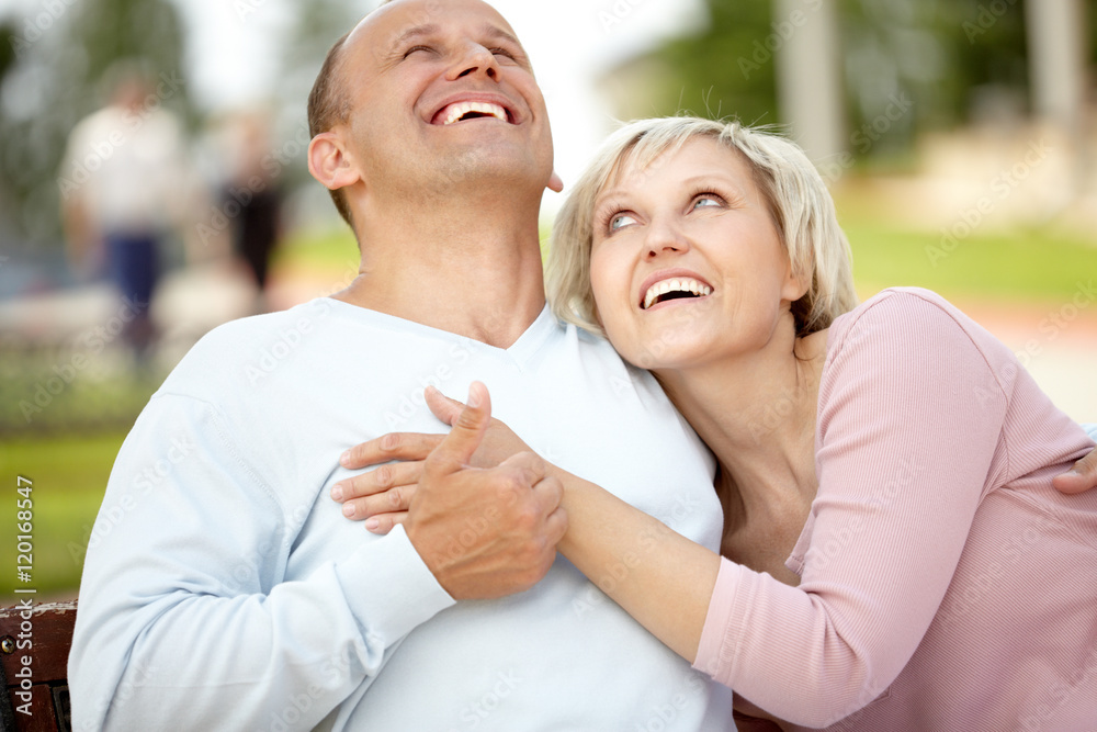 Mature couple embracing on bench and laughing Mature couple embracing on bench and laughing
