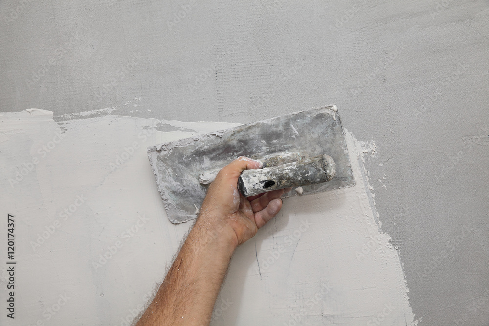 Worker spreading plaster to wall, closeup of hand and trowel tool Worker spreading plaster to wall, closeup of hand and trowel tool