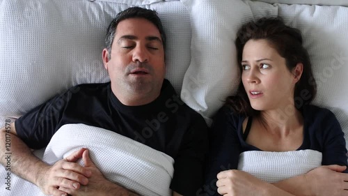 Woman (age 30-40) suffers from her partner (age 35 - 45) snoring in bed. Couple lifestyle and people health care concept. Real people copy space photo