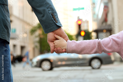 father holding the daughter/ child hand behind the traffic l