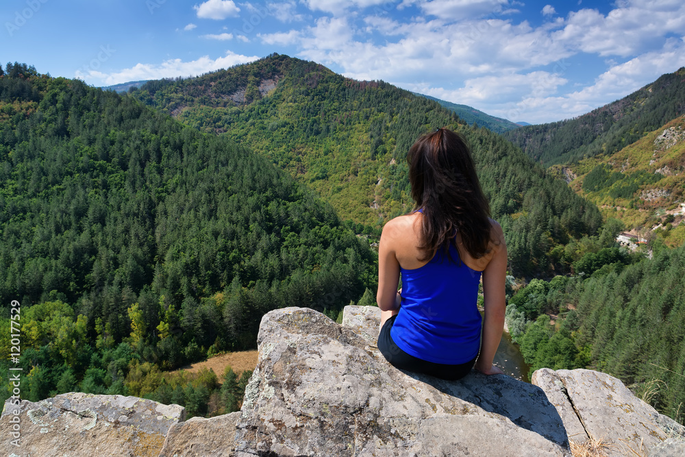 Naklejka premium A girl is sitting on the edge of a cliff and looking at a mountain