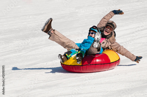 Winter fun. Young woman and little boy sliding downhill on a snow tube