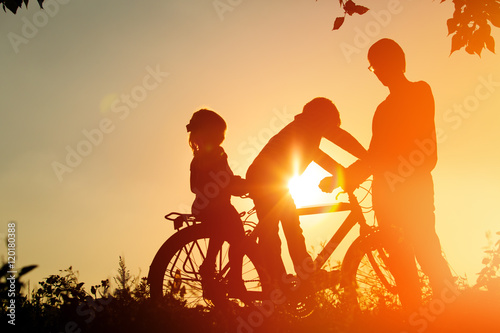 father with two kids riding bike at sunset