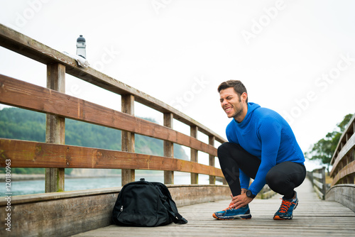 Fit runner sportsman holding ankle in pain in a park. Broken twisted joint running sport injury. Athletic man touching foot due to sprain.
