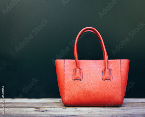 Fashionable beautiful big red handbag standing on a wooden floor on black wall background. Still life. Warm color