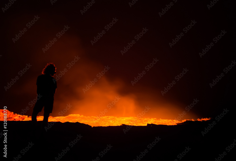 Fototapeta premium Person standing at the edge of Erta Ale active volcano at night
