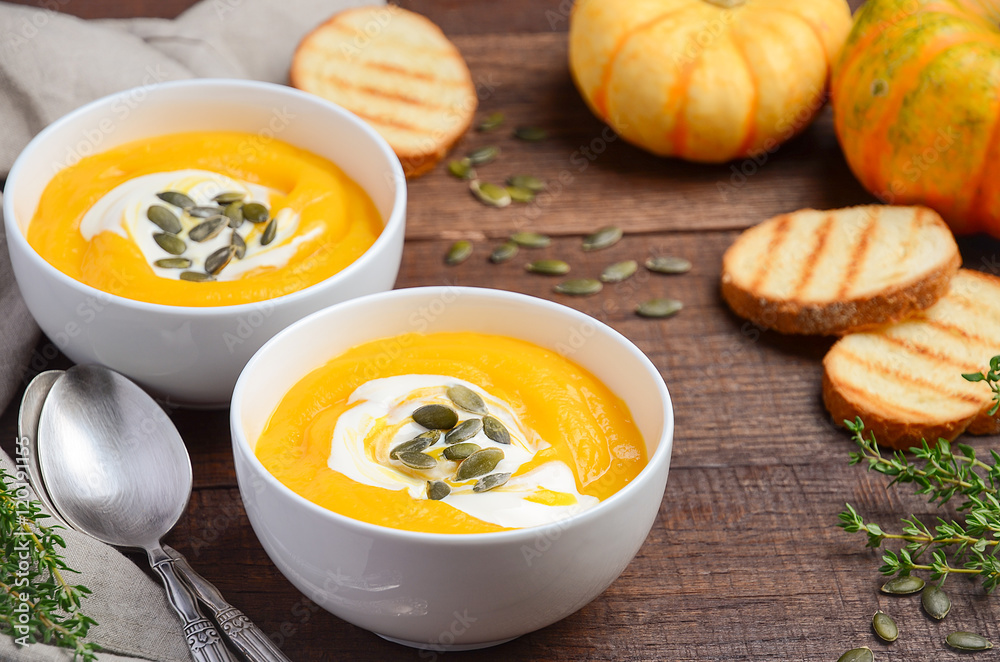 Pumpkin cream soup with cream and pumpkin seeds on wooden background, selective focus Pumpkin cream soup with cream and pumpkin seeds on wooden background, selective focus