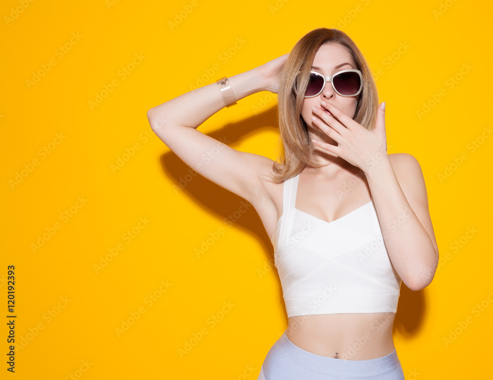 Beautiful fashionable girl posing in a skirt and top with sunglasses on a yellow background covering her mouth with his hand. Gorgeous Woman Portrait. Sexy Glamour Girl on Yellow background Beautiful fashionable girl posing in a skirt and top with sunglasses on a yellow background covering her mouth with his hand. Gorgeous Woman Portrait. Sexy Glamour Girl on Yellow background