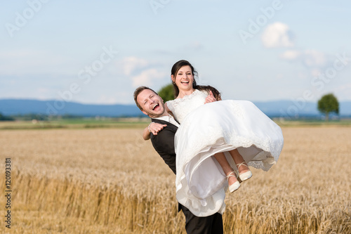 Bräutigam trägt Braut auf Händen, im Freien, beide lachen
