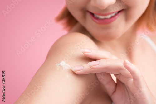 Woman use body lotion on arms and touching her skin on pink back