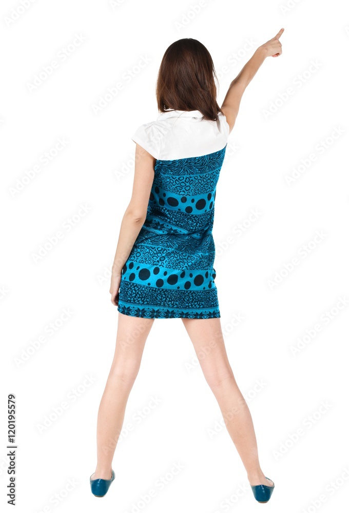 Fototapeta premium Back view of young brunette woman pointing at wall . beautiful girl in blue dress showing gesture. Rear view. Isolated over white background.