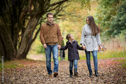 Lovely family walking in the autumn forest. Happy parents enjoying fresh air and beautiful nature, holding hands, talking, smiling and laughing. Healthy lifestyle