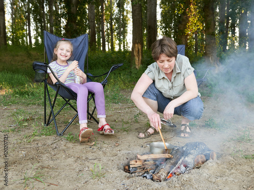 woman cooking food, people camping in forest, family active in nature, child girl sit in travel seat, summer season