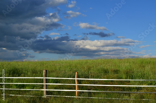 Landscape image of countryside with field of green grass, fence and blue sky with clouds