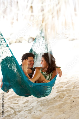 This young couple have fun In a hammock on vacation, under a palapa, cabana on the beach in central america