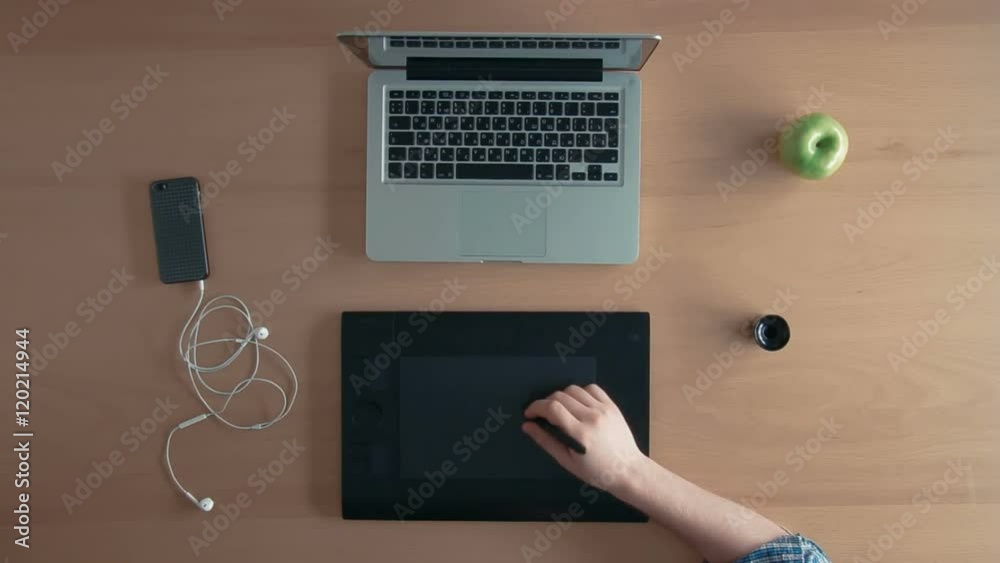 Top view designer man or illustrator uses his graphics tablet and laptop creating digital design and eats an apple