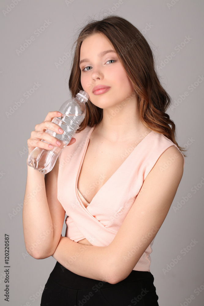 Girl touching her face by bottle of water. Close up. Gray background Girl touching her face by bottle of water. Close up. Gray background