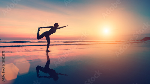 Silhouette of woman doing exercises on the sea beach during sunset.