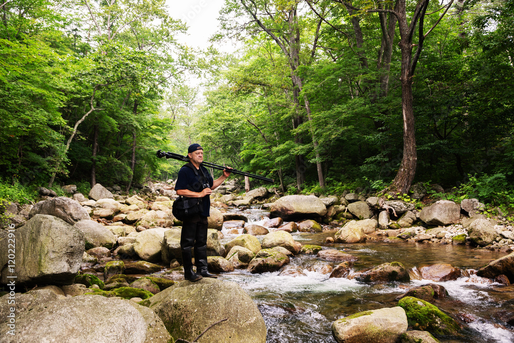 Photographer with camera travels across mountain river Photographer with camera travels across mountain river