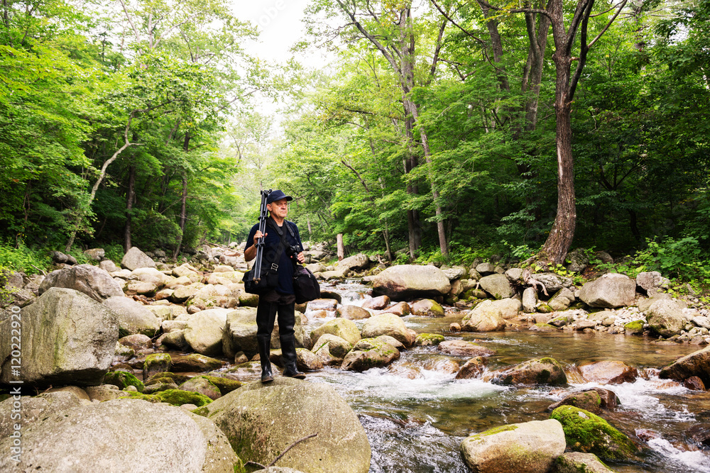 Photographer with camera travels across mountain river Photographer with camera travels across mountain river