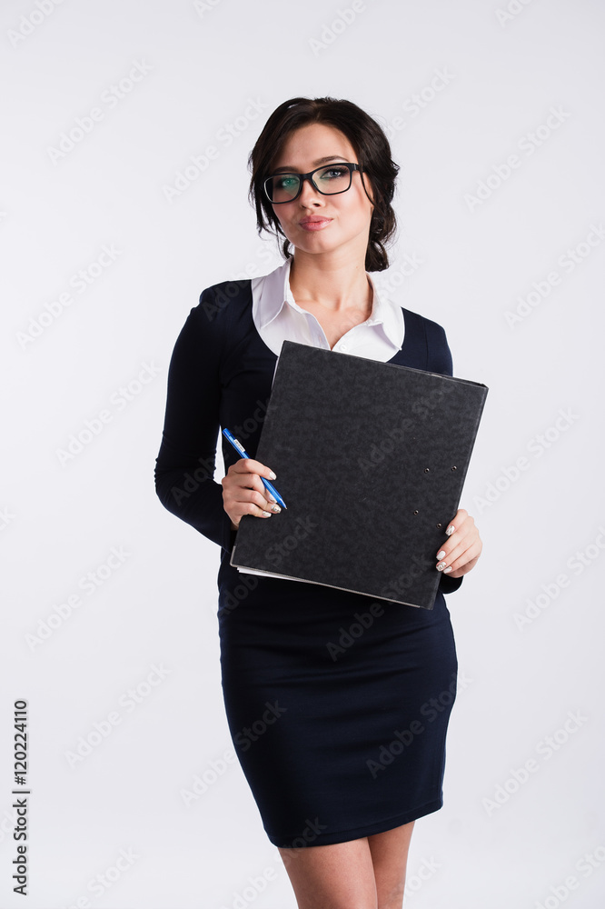 Young Caucasian woman wearing dark blue dress, white shirt, holding a ring binder folder and pen. Isolated on light background. Young Caucasian woman wearing dark blue dress, white shirt, holding a ring binder folder and pen. Isolated on light background.