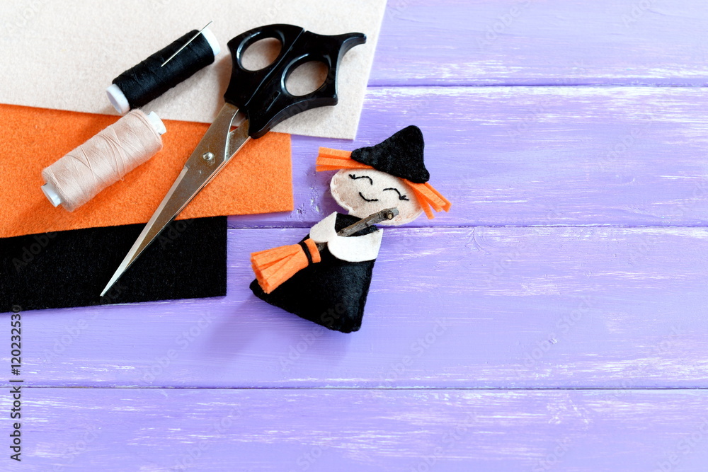 Adorable Halloween witch made of felt, scissors, thread set, orange, beige  and black felt sheets on wooden background with copy space for text.  Halloween crafts idea for kids. Inspiration crafts Stock Photo