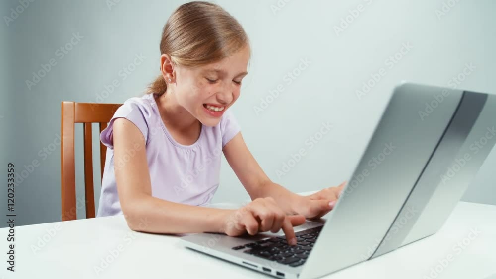 Girl 7-8 years using laptop with smile and then shocked information online. Child closing laptop Girl 7-8 years using laptop with smile and then shocked information online. Child closing laptop