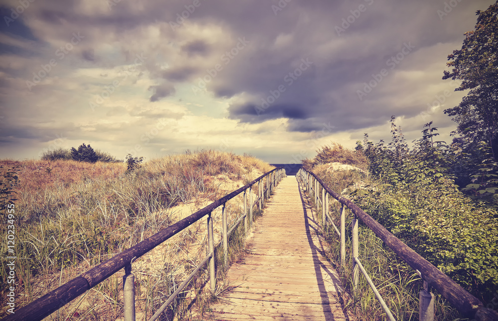 Vintage toned wooden footpath leading to a beach, rainy clouds in distance.