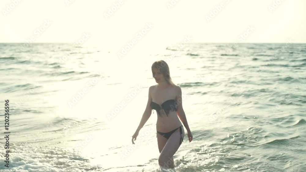 Young beautiful girl in swimwear smiling, walking on sea at sunrise Young beautiful girl in swimwear smiling, walking on sea at sunrise