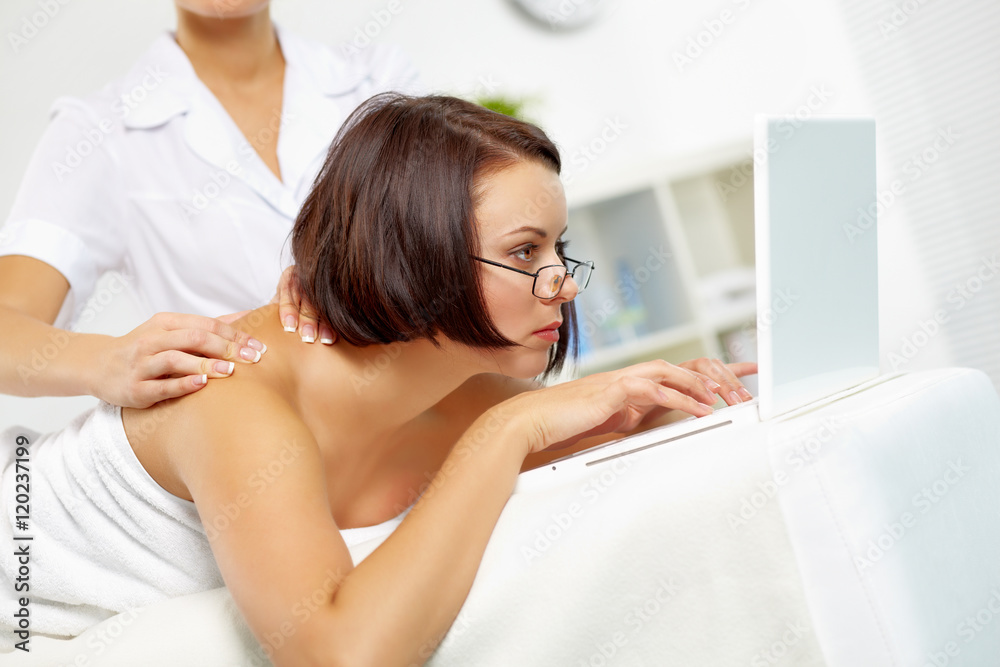 Young businesswoman lying on massage table and working on computer Young businesswoman lying on massage table and working on computer