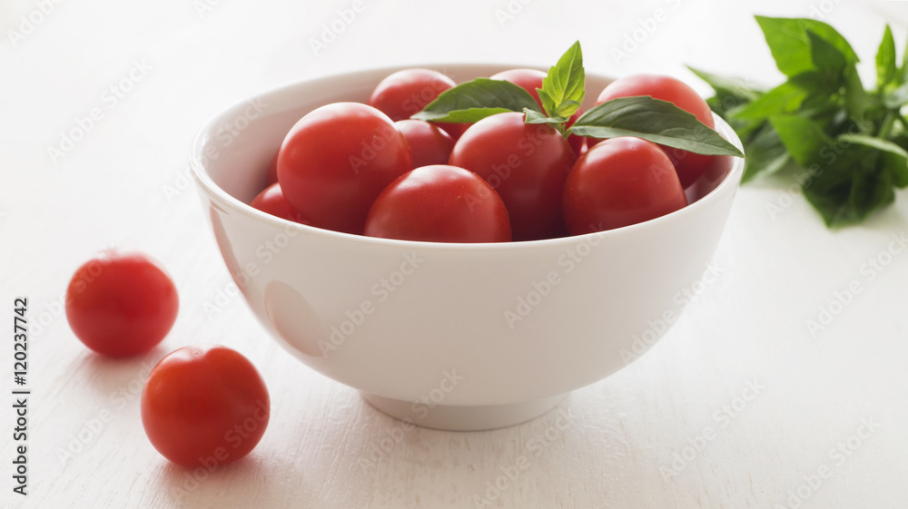 Fresh cherry tomatoes with basil leaves in white bowl Fresh cherry tomatoes with basil leaves in white bowl