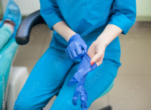 Close-up of dentist female putting on blue disposable gloves. Focus on the her hands with red manicure