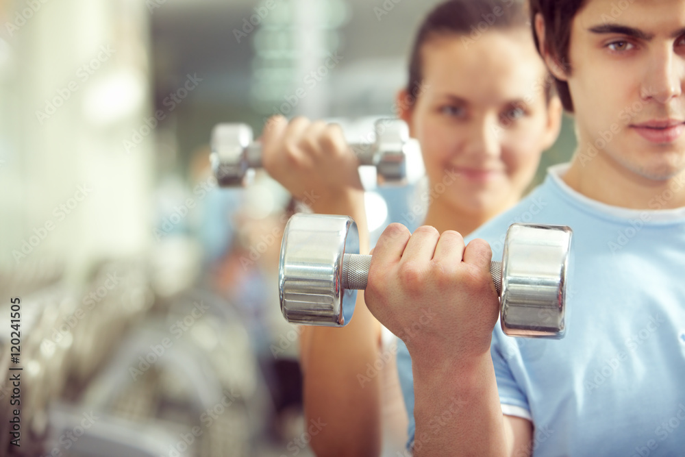Young man picking up a dumbbell with woman on background Young man picking up a dumbbell with woman on background