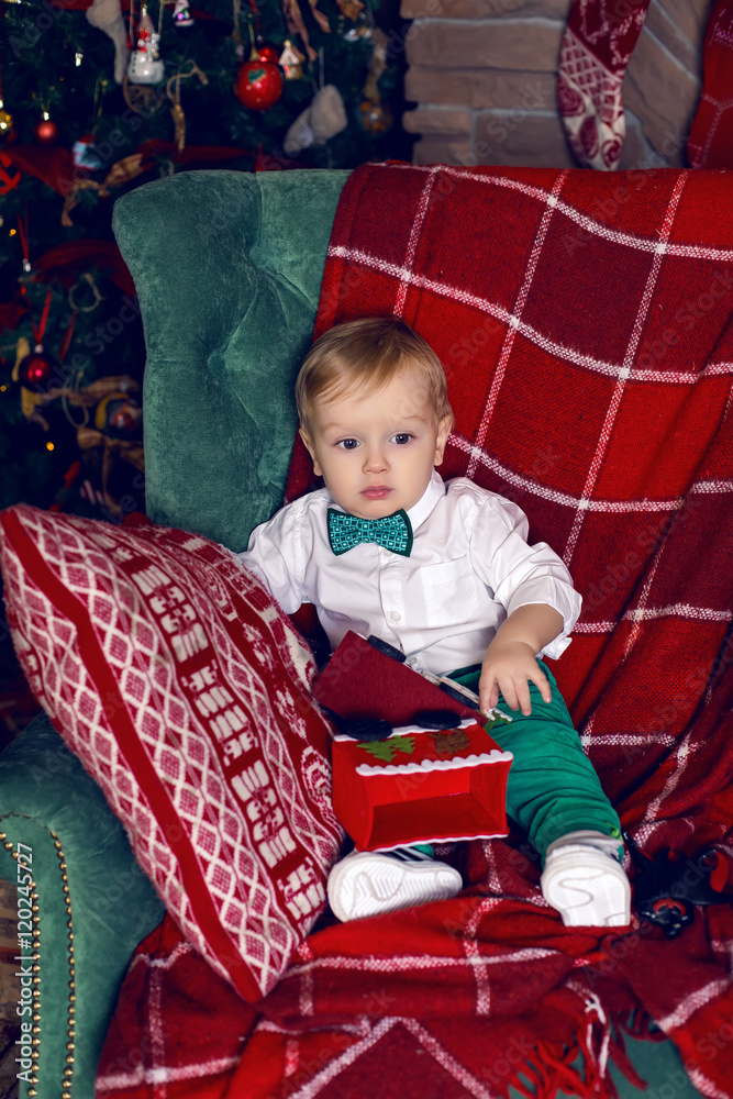 small child sits on the chair near the Christmas tree small child sits on the chair near the Christmas tree
