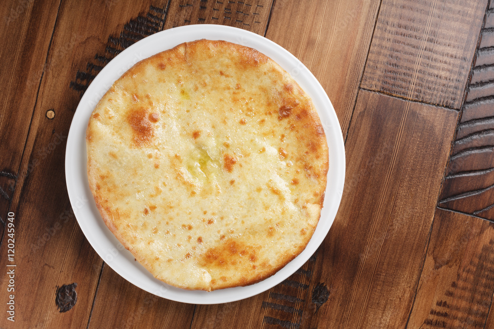 Ossetian pie with potatoes or mutton on a white plate. Wooden background. Ossetian pie with potatoes or mutton on a white plate. Wooden background.