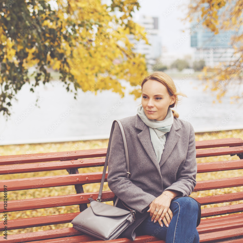 Fototapeta premium Young woman in grey coat sitting on a bench