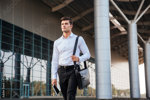 Portrait of a confident young businessman walking with pc tablet