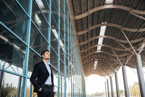 Confident handsome businessman standing with glass building on background