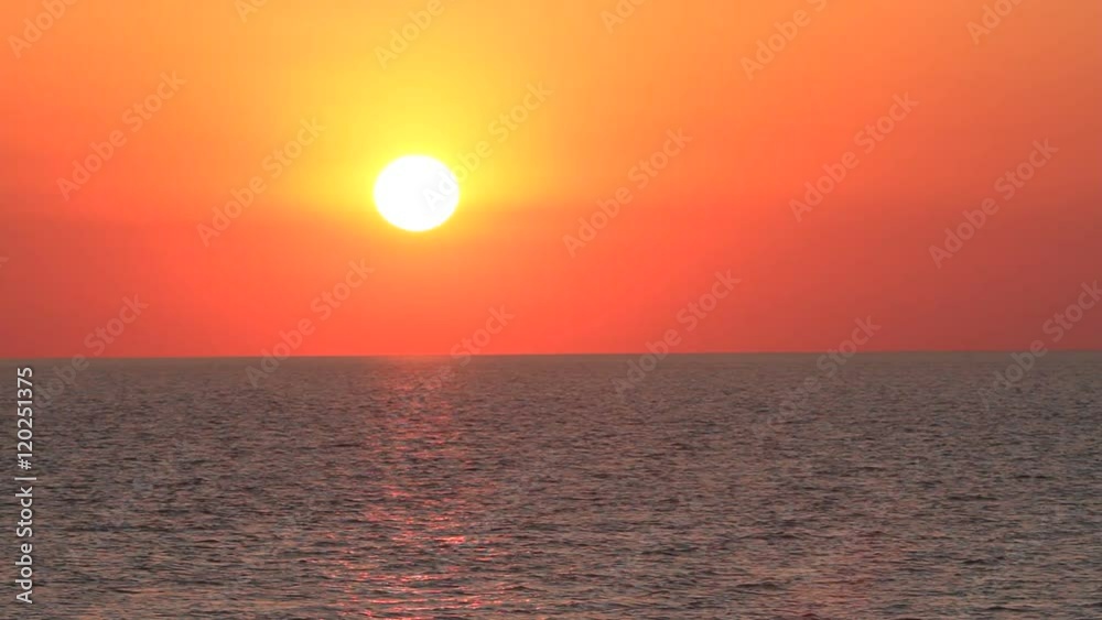 Sunset on a sea with white sun disc, red sky and dark blue or grey wavy water surface with the sun reflections. Sunset on a sea with white sun disc, red sky and dark blue or grey wavy water surface with the sun reflections.